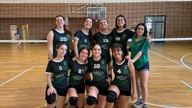 Equipo femenino de voleibol del CV Huesca posando en un pabellón deportivo junto a una integrante de TEAM CO